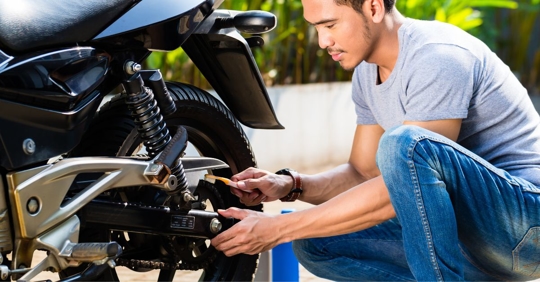 man bent down cleaning his motorcycle chain with a toothbrush