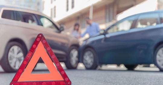 Close up of a orange triangle on the ground, with a car accident in the background