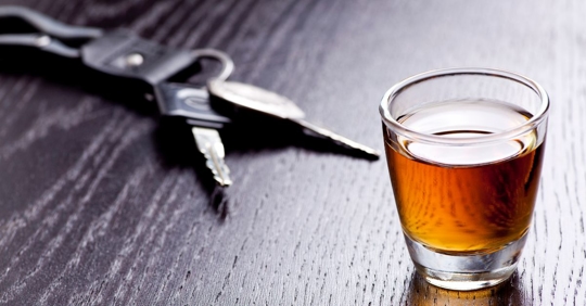 a glass of dark-colored liquid sitting on a wooden table next to car keys
